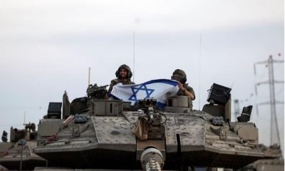 Israeli soldiers hold an Israeli flag while in a tank near Israel's border with the Gaza Strip