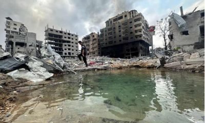 A Palestinian walks through the rubble while smoke rises from a damaged residential building nearby, in the aftermath of Israeli strikes, in Gaza City